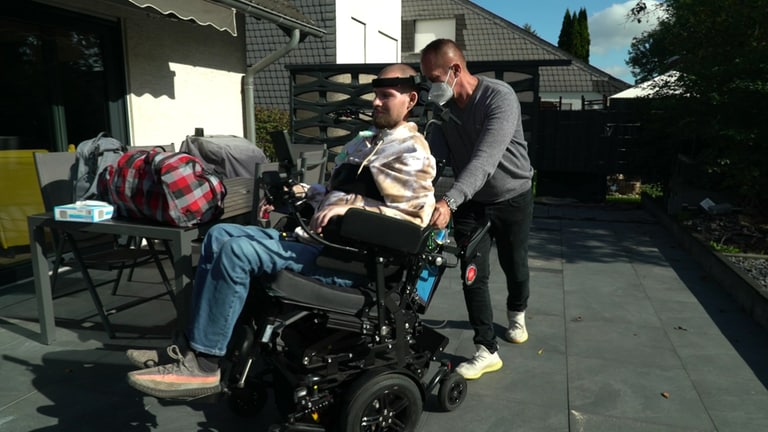 Älterer Mann schiebt jungen Mann im Rollstuhl
