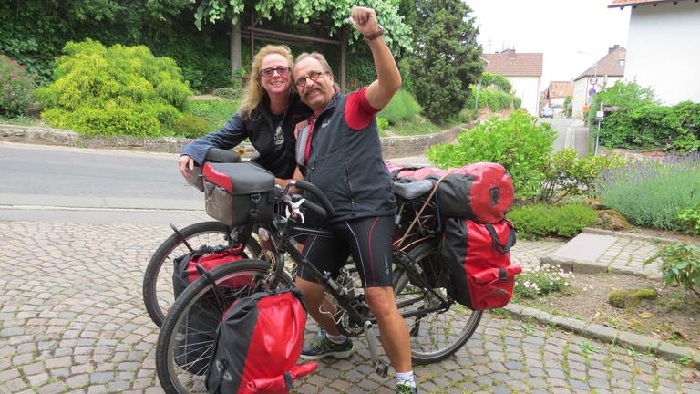 Eine Frau und ein Mann in Fahrradkleidung mit ihren bepackten Fahrrädern.