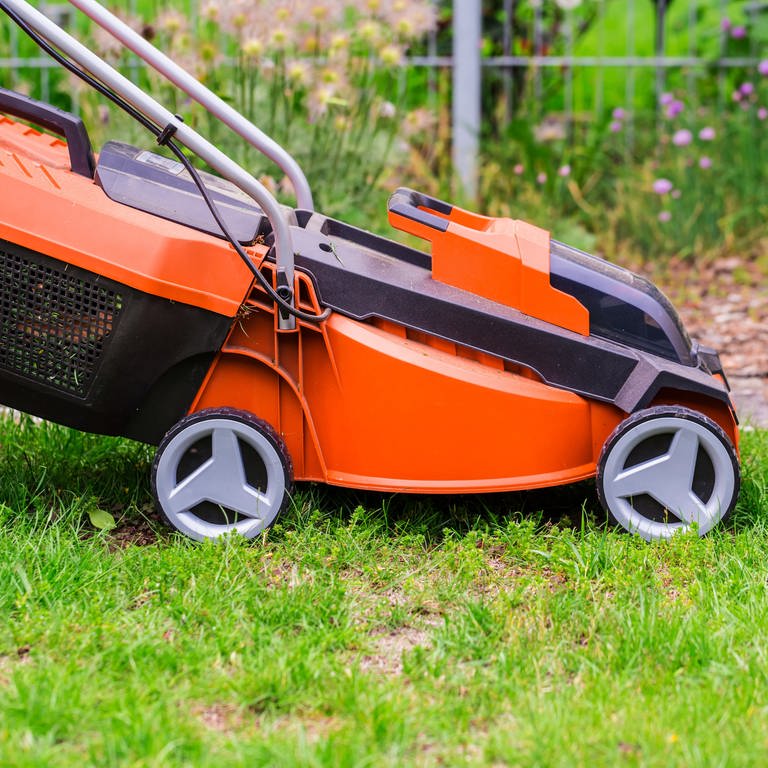 Nachbarschaftslärm durch Rasenmäher: Hier ist ein orangefarbener Rasenmäher in Großaufnahme zu sehen, der auf einem Rasen steht.