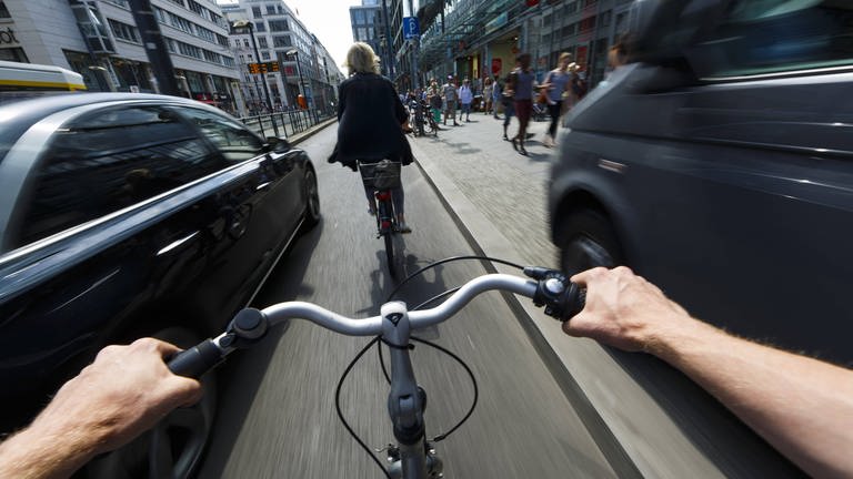 Ein Radfahrer wird im Stadtverkehr von einem nah vorbeifahrenden Auto überholt.