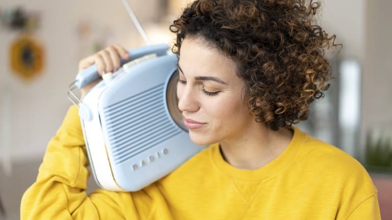 Frau im gelben Pulli hört entspannt Radio