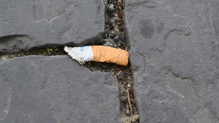 Ein achtlos weggeworfener und nasser Zigarettenstummel auf dem Boden. Er enthält schädliche Chemikalien und Mikroplastik -  all dass wird ausgewaschen und gelangt so ins Grundwasser.