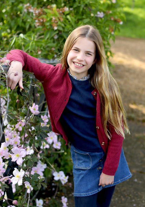 Prinzessin Charlotte stützt den rechten Arm auf ein mit Blumen überrankten Zaun: Die Tochter von Prinzessin Kate und Prinz William feiert ihren 9. Geburtstag.