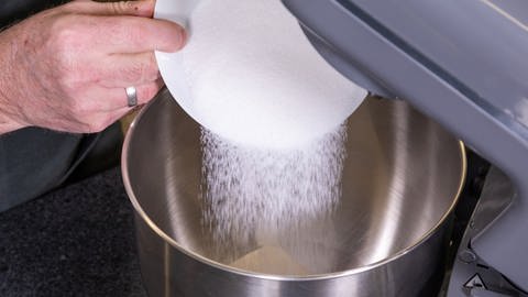 Zucker für den Teig wird in die Rührschüssel gegeben. Dann wird laut Rezept der Kuchenteig für den Kuchen im Glas einige Zeit gerührt.