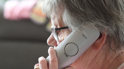 Eine ältere Frau mit grauen kurzen Haaren hält den Telefonhörer ans Ohr