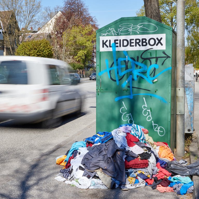 Ein Kleiderberg liegt vor einem Altkleidercontainer mit der Aufschrift «Kleiderbox» am Straßenrand
