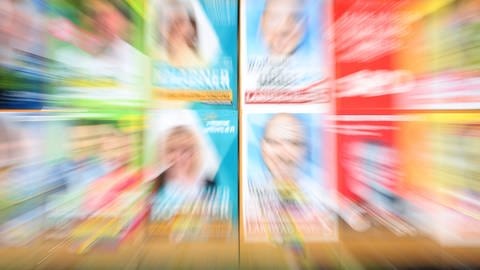 Eine Plakatwand zeigt verschwommen Plakate verschiedener Parteien zur bayerischen Landtagswahl 2023. 