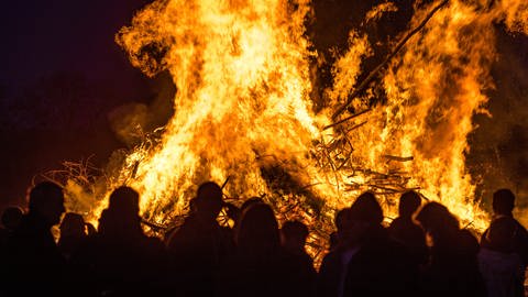 Menschen stehen vor einem brennenden Osterfeuer.