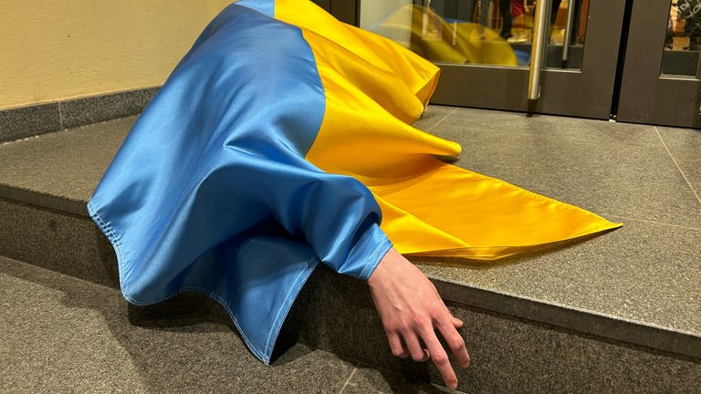 Eine ukrainische Flagge bedeckt einen Menschen am Boden.