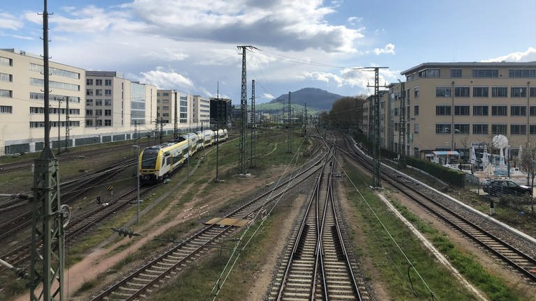 Blick auf den Schönberg, im Vordergrund liegen viele Zuggleise. Auf einem fährt ein gelber Zug, der Breisgau-S-Bahn.
