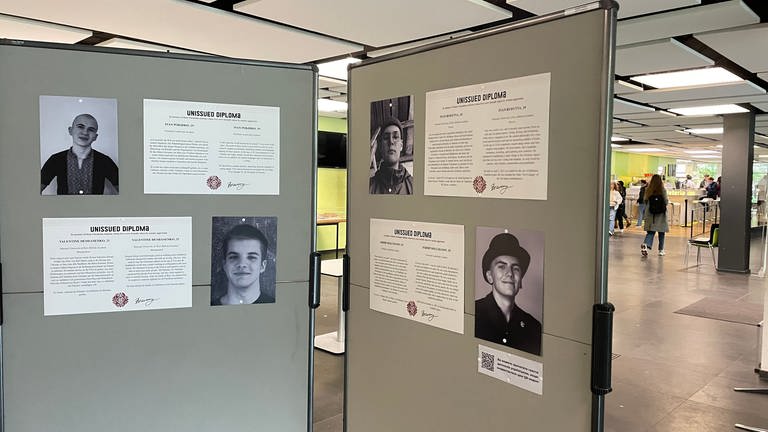 Eine Stellwand mit vier Porträts von jungen Männern in der Ausstellung "Unissued Diplomas". Sie zeigt in der Universitätsbibliothek Fotos von jungen Menschen, die im Krieg in der Ukraine gestorben sind. (Foto: SWR, Peter Binder)