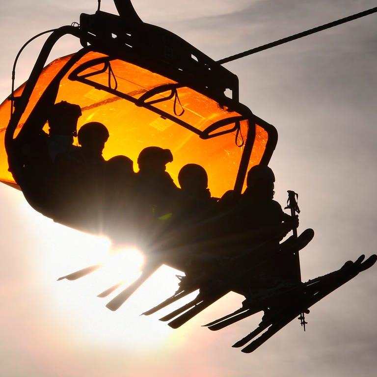 Skifahrer benutzen einen großen Sessellift in einem Skigebiet, während die Sonne tief steht.