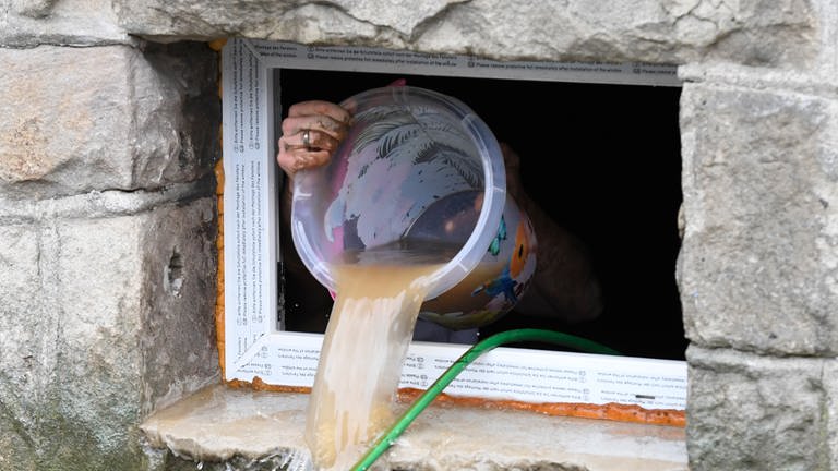 Ein Frau schöpft mit einem Einmer Wasser aus einem überfluteten Keller. 