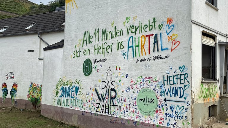 Auf einer Hauswand in Dernau steht der Spruch: "Alle elf Minuten verliebt sich ein Helfer ins Ahrtal". 