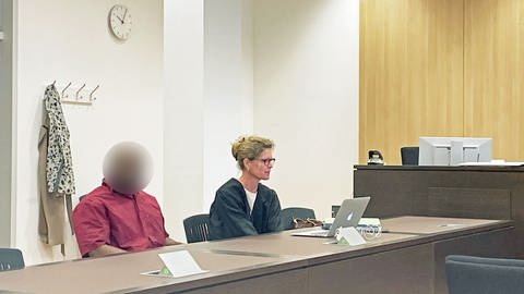Ein Mann sitzt neben seiner Anwältin auf der Anklagebank