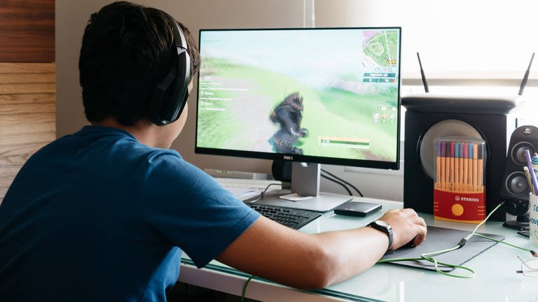 Ein Jugendlicher am Schreibtisch sitzend und spielt ein Computerspiel