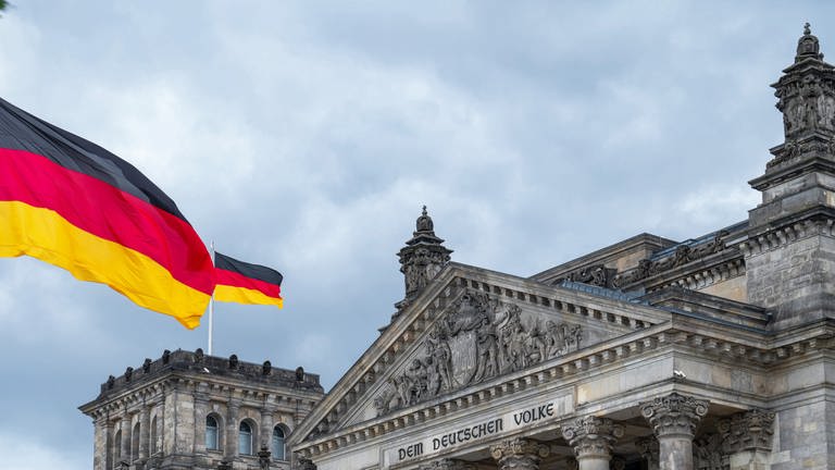 Bundesflagge der Bundesrepublik Deutschland mit den Farben schwarz, rot, gold weht vor und auf dem Reichstagsgebäude in Berlin