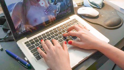 Hände mit lackierten Fingernägeln auf Tastatur eines Laptops, auf dem ein Porno läuft: Mädchen und Frauen sind noch nicht gleichberechtigt, sie haben mit unzeitgemäßen Erwartungen von Jungs und Männern zu kämpfen, die diese aus Pornos übernehmen