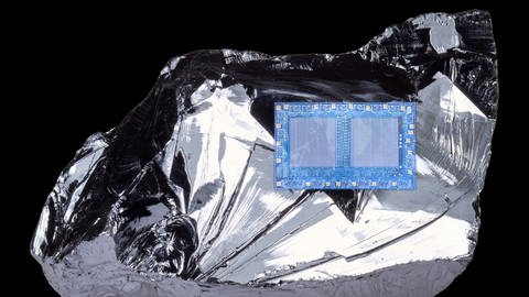 Auf einem unförmigen Stück metallisch glänzendem Silizium liegt ein bläulicher Mikrochip.